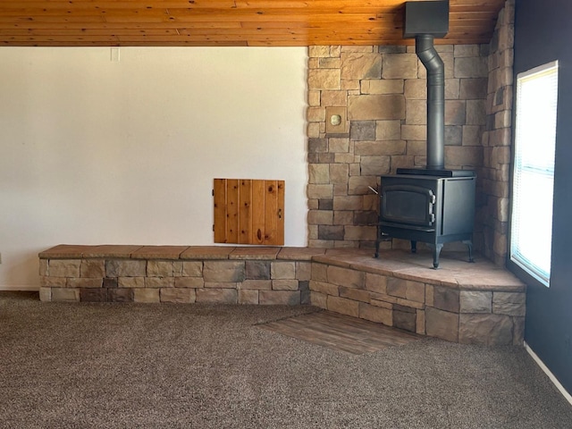 basement featuring a wood stove, carpet flooring, wood ceiling, and plenty of natural light