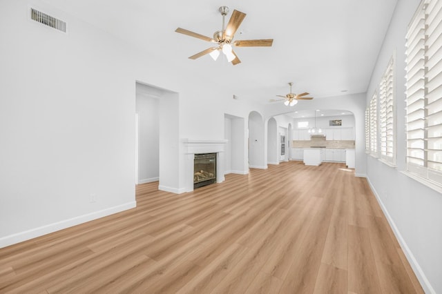 unfurnished living room with visible vents, a ceiling fan, a glass covered fireplace, light wood finished floors, and baseboards