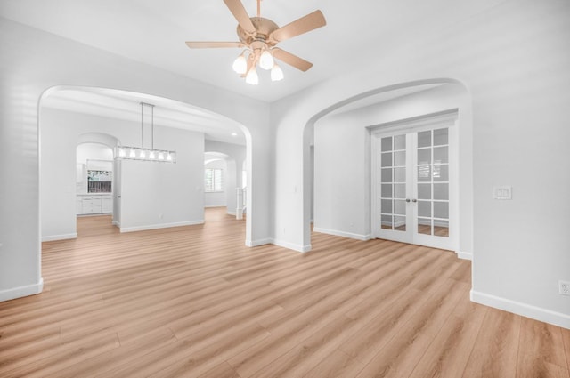 unfurnished living room featuring baseboards, arched walkways, light wood-style flooring, and a ceiling fan