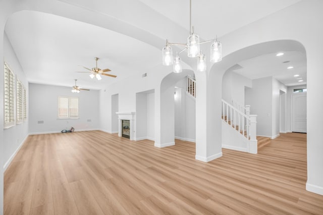 unfurnished living room featuring arched walkways, a glass covered fireplace, stairs, and light wood finished floors