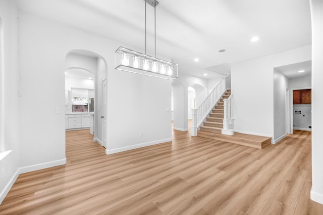 unfurnished dining area with arched walkways, light wood-type flooring, stairs, and baseboards