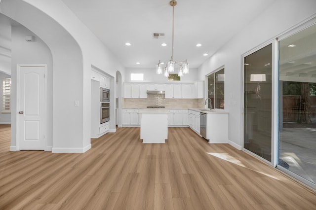 kitchen with under cabinet range hood, a sink, backsplash, arched walkways, and appliances with stainless steel finishes