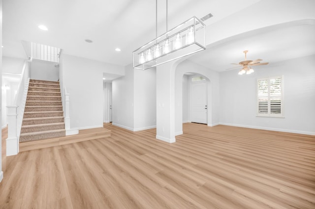 unfurnished living room with baseboards, stairs, light wood-style flooring, arched walkways, and a ceiling fan