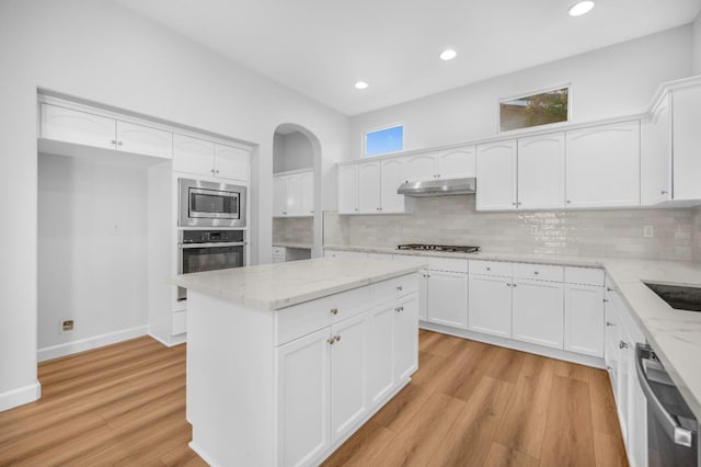 kitchen featuring light stone countertops, under cabinet range hood, decorative backsplash, light wood-style flooring, and stainless steel appliances