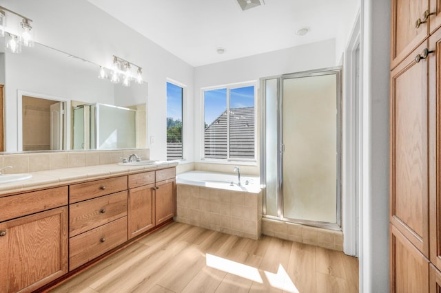 full bathroom with a shower stall, double vanity, wood finished floors, a bath, and a sink