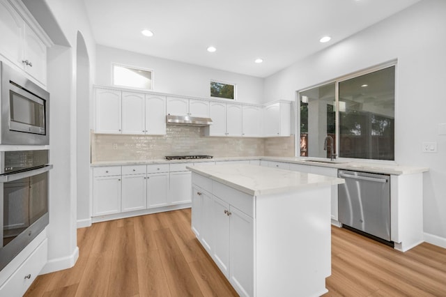 kitchen with under cabinet range hood, light wood-type flooring, white cabinets, stainless steel appliances, and a sink