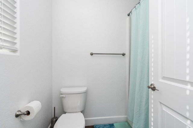 bathroom featuring curtained shower, toilet, and baseboards