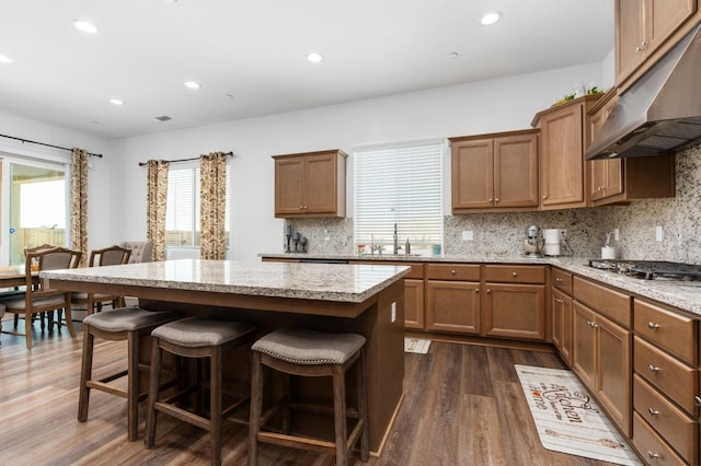 kitchen with dark wood-style flooring, a sink, under cabinet range hood, a kitchen breakfast bar, and a center island