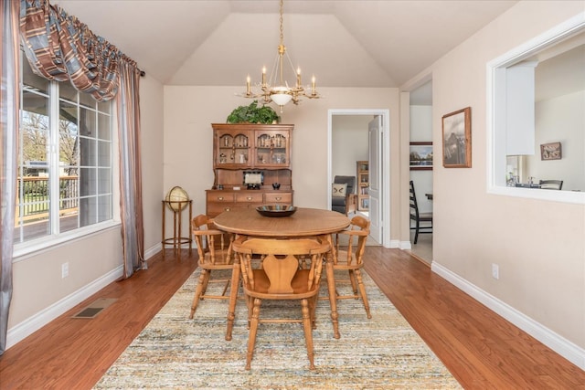 dining area with a notable chandelier, visible vents, lofted ceiling, and wood finished floors