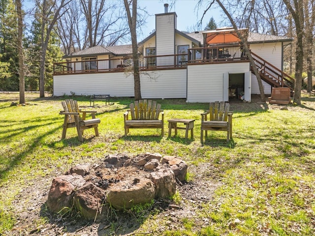 rear view of house featuring an outdoor fire pit, a wooden deck, a yard, a chimney, and stairs