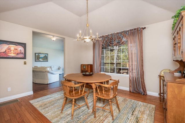 dining area featuring a chandelier, baseboards, lofted ceiling, and wood finished floors