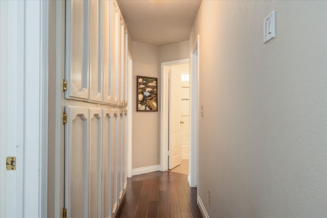 corridor featuring baseboards and dark wood-style floors