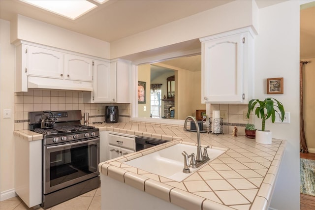 kitchen featuring gas stove, backsplash, under cabinet range hood, and white cabinetry