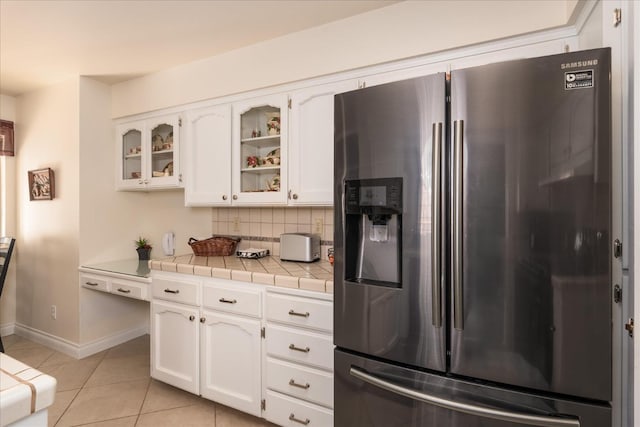 kitchen featuring tasteful backsplash, glass insert cabinets, stainless steel fridge with ice dispenser, light tile patterned floors, and white cabinetry