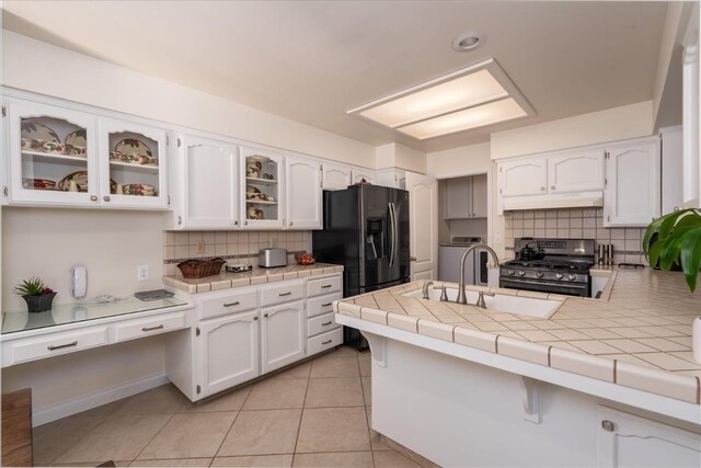 kitchen with a sink, white cabinets, black refrigerator with ice dispenser, and stainless steel gas range oven