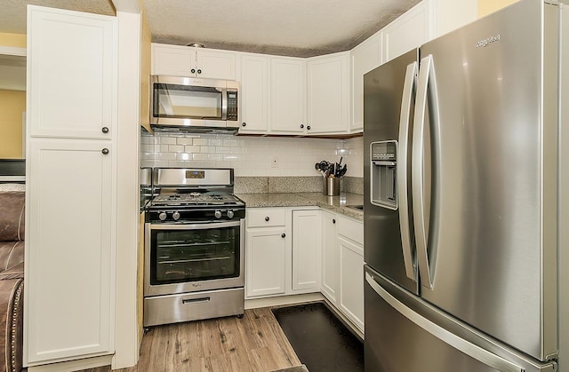 kitchen featuring light stone counters, wood finished floors, white cabinets, appliances with stainless steel finishes, and tasteful backsplash