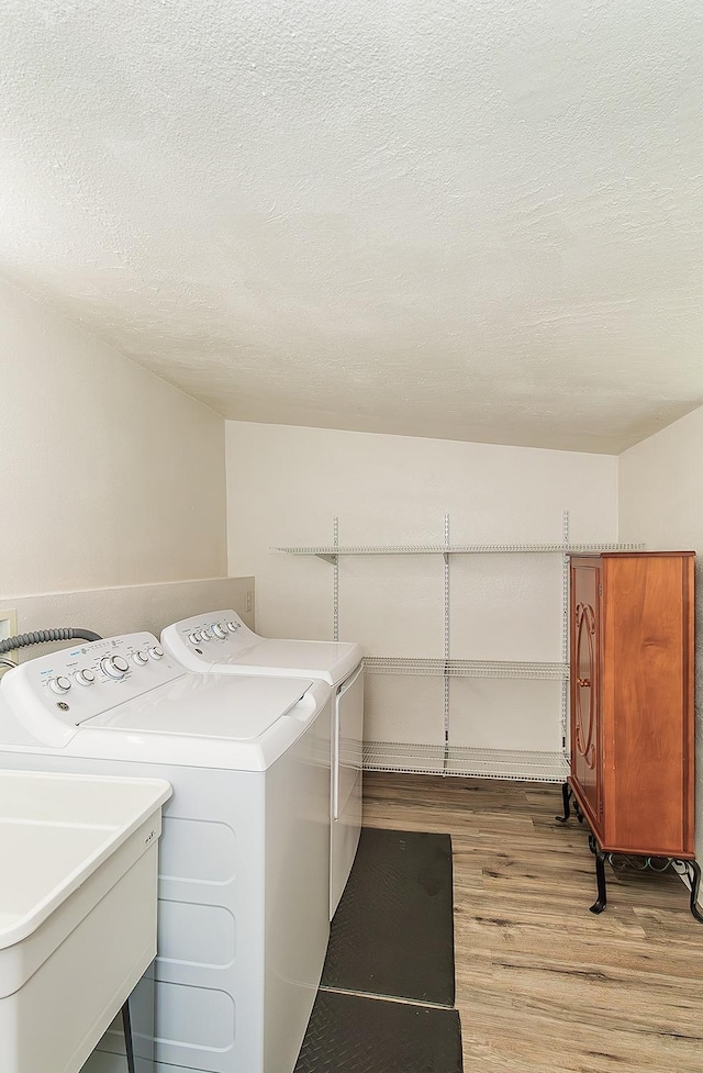 laundry room featuring washing machine and clothes dryer, laundry area, a sink, a textured ceiling, and light wood-type flooring