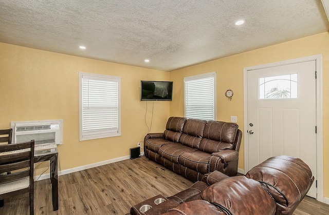 living area with an AC wall unit, a textured ceiling, wood finished floors, recessed lighting, and baseboards