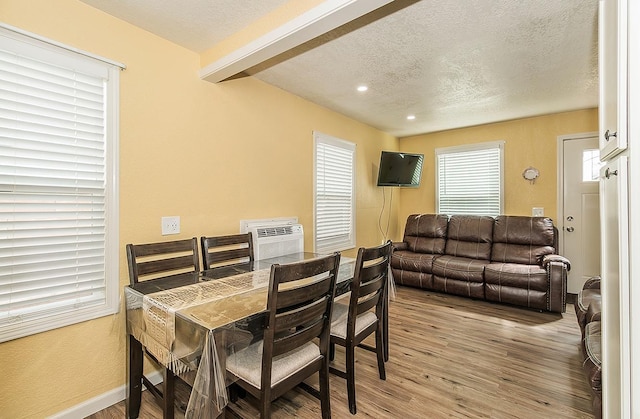 dining space featuring a wall mounted AC, a textured ceiling, light wood-type flooring, and baseboards