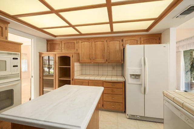 kitchen featuring visible vents, tile countertops, white appliances, light tile patterned floors, and decorative backsplash