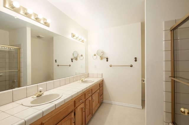 bathroom featuring a sink, baseboards, tiled shower, and double vanity