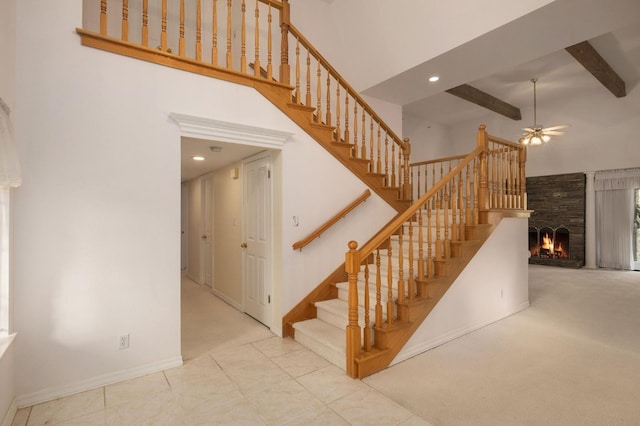 staircase with beamed ceiling, a ceiling fan, a large fireplace, a high ceiling, and baseboards