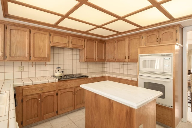 kitchen featuring white appliances, light tile patterned flooring, tile counters, tasteful backsplash, and a center island