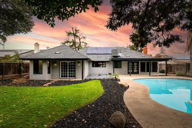 back of property featuring roof mounted solar panels, a lawn, a chimney, a fenced backyard, and a patio