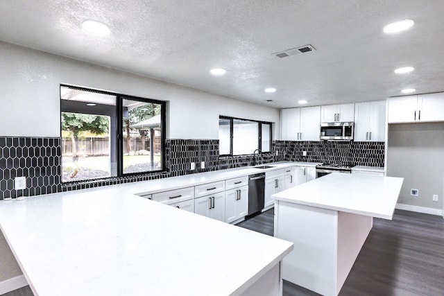 kitchen with visible vents, a sink, stainless steel appliances, a peninsula, and white cabinets