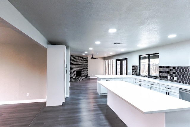 kitchen featuring white cabinets, a peninsula, light countertops, and dark wood-style flooring