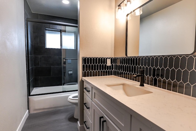 bathroom featuring tasteful backsplash, bath / shower combo with glass door, toilet, wood finished floors, and vanity