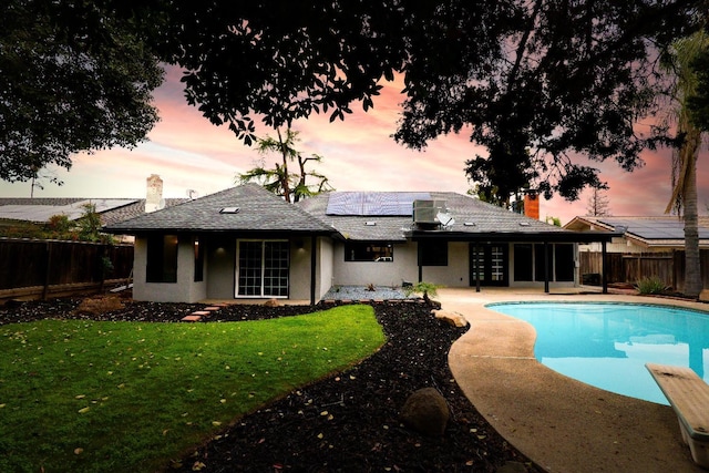 back of property featuring a yard, roof mounted solar panels, a fenced in pool, and a fenced backyard