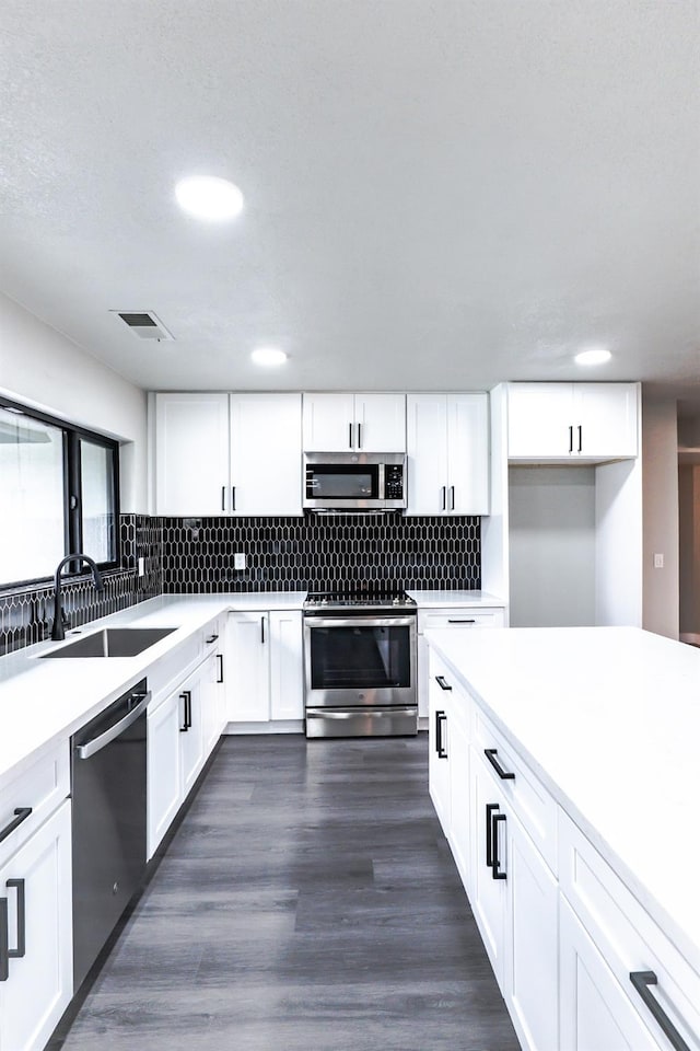 kitchen featuring visible vents, a sink, decorative backsplash, dark wood-type flooring, and appliances with stainless steel finishes