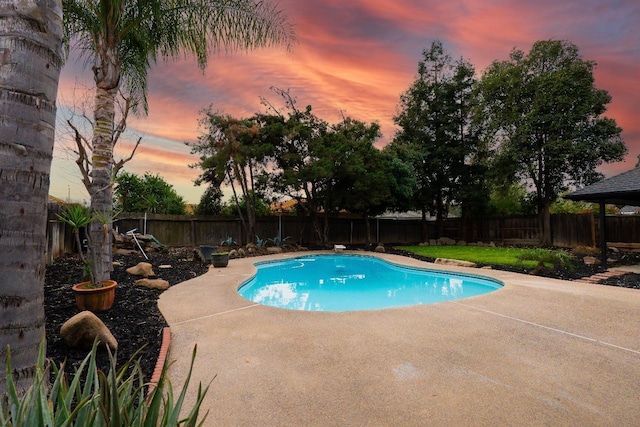 pool at dusk featuring a patio area, a fenced in pool, and a fenced backyard