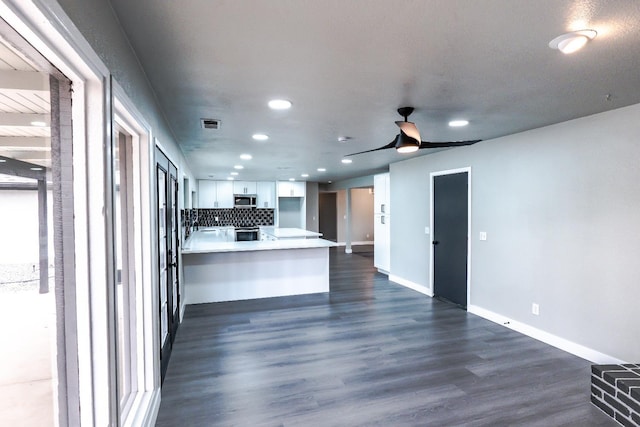 kitchen featuring dark wood-style floors, a peninsula, decorative backsplash, white cabinets, and stainless steel microwave