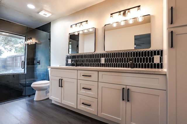 full bathroom with visible vents, toilet, a stall shower, wood finished floors, and double vanity