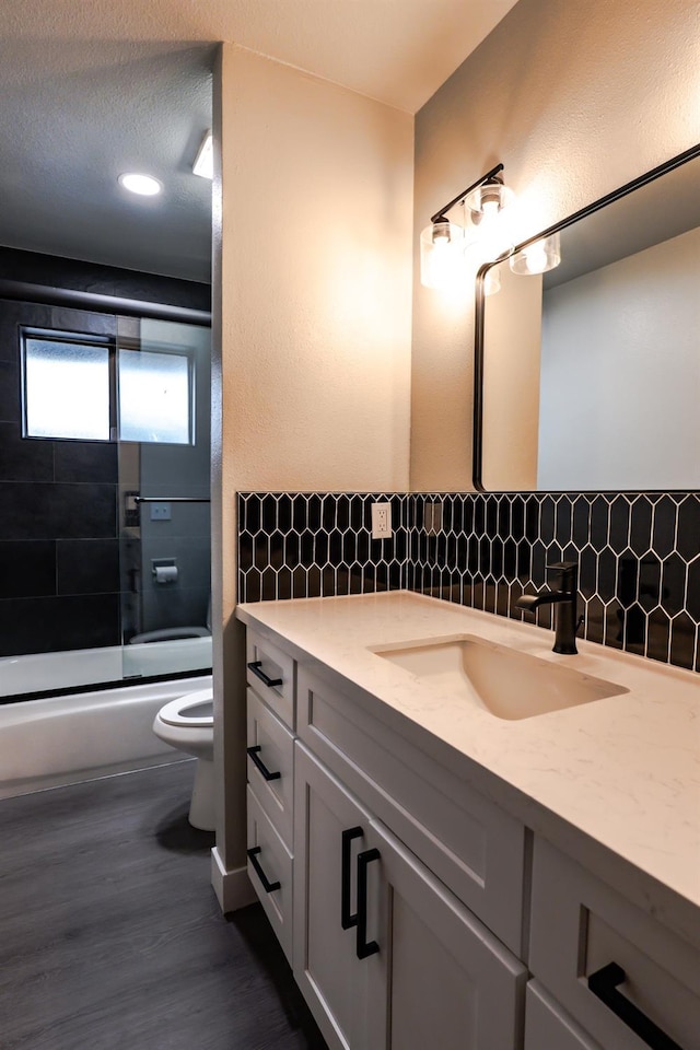 bathroom featuring toilet, tasteful backsplash, wood finished floors, bath / shower combo with glass door, and vanity