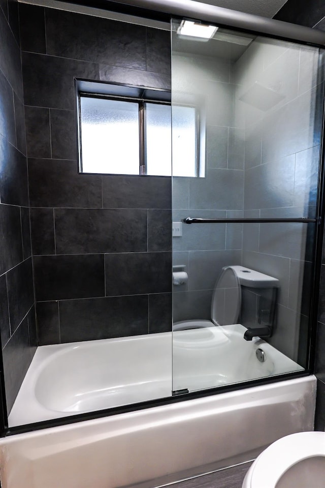 bathroom featuring toilet and bath / shower combo with glass door