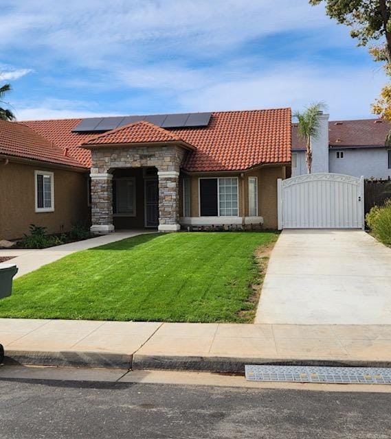 mediterranean / spanish-style house featuring roof mounted solar panels, a tile roof, a front lawn, and a gate