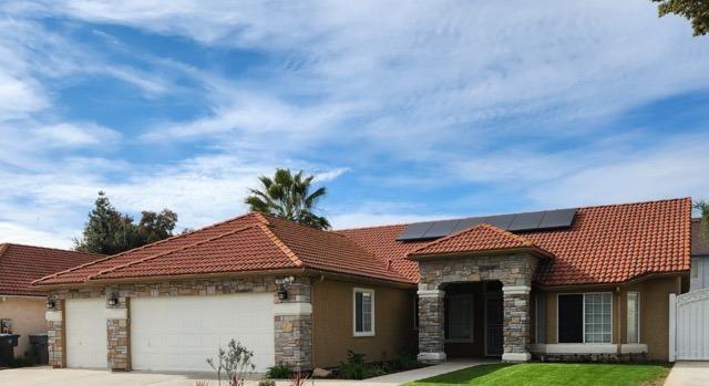 mediterranean / spanish house featuring solar panels, a tile roof, a garage, stone siding, and driveway