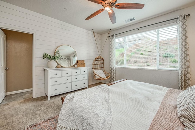 carpeted bedroom with wooden walls, visible vents, and a ceiling fan