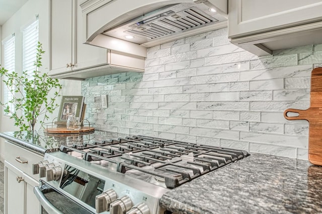 kitchen featuring dark stone countertops, white cabinetry, gas stove, decorative backsplash, and custom exhaust hood