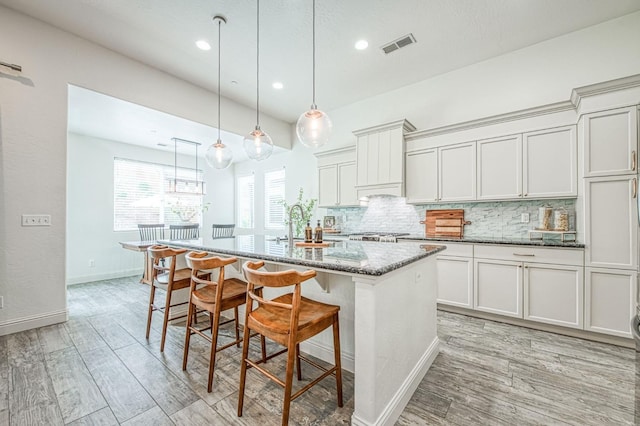 kitchen featuring dark stone countertops, visible vents, light wood finished floors, a kitchen breakfast bar, and backsplash