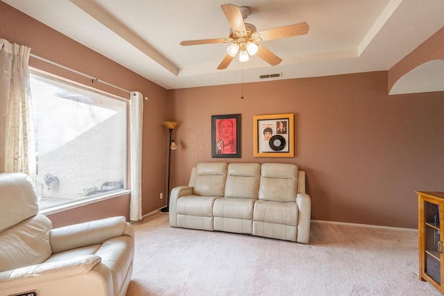 living room with visible vents, baseboards, ceiling fan, a tray ceiling, and carpet flooring