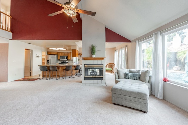 living room featuring baseboards, high vaulted ceiling, a fireplace, ceiling fan, and light carpet