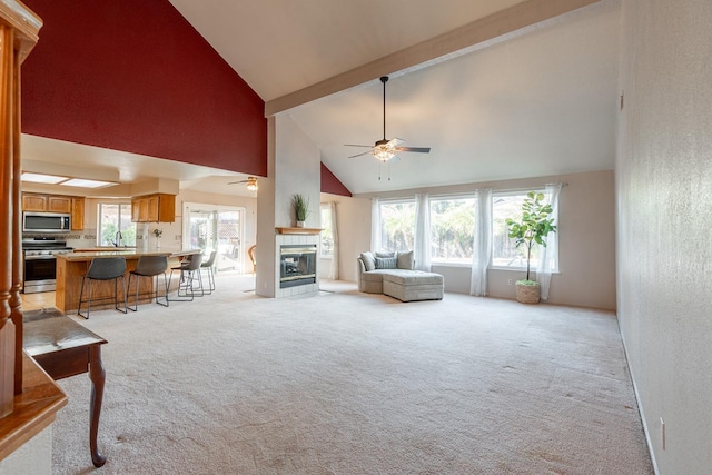 living area with a tiled fireplace, plenty of natural light, light colored carpet, and beam ceiling