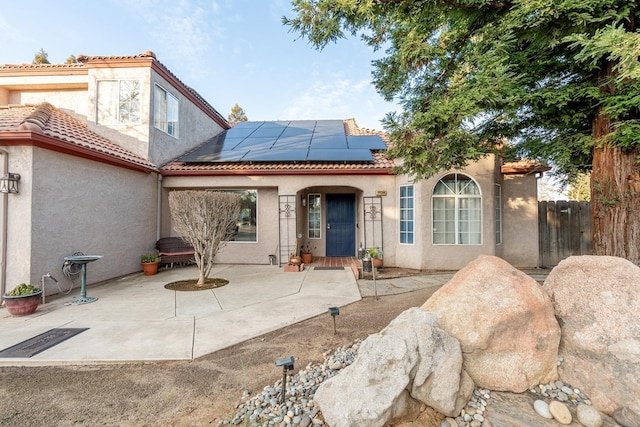 rear view of property with stucco siding, a patio, roof mounted solar panels, fence, and a tiled roof