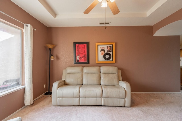 carpeted living area featuring a raised ceiling, a ceiling fan, visible vents, and baseboards