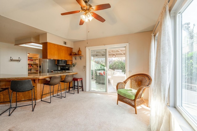 kitchen featuring visible vents, brown cabinets, a breakfast bar, appliances with stainless steel finishes, and light colored carpet