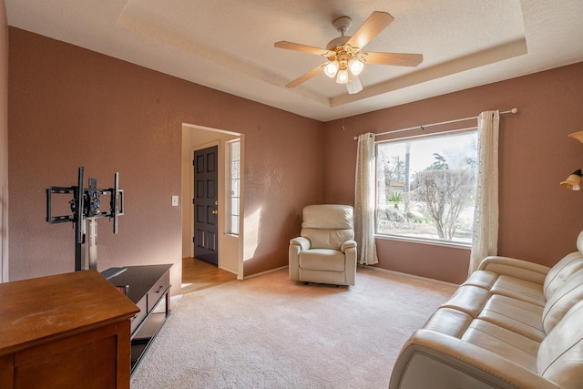 living area featuring baseboards, a raised ceiling, light carpet, and a ceiling fan